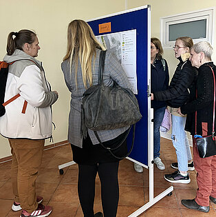 Gruppe von fünf Personen, die an einer Stellwand stehen und auf eine Präsentation schauen.