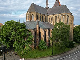 Marienkirche mit gotischer Architektur, umgeben von Bäumen und einem Gehweg unter bewölktem Himmel.