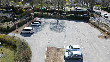 Parkplatz mit fünf geparkten Autos, umgeben von Bäumen und einem Zaun