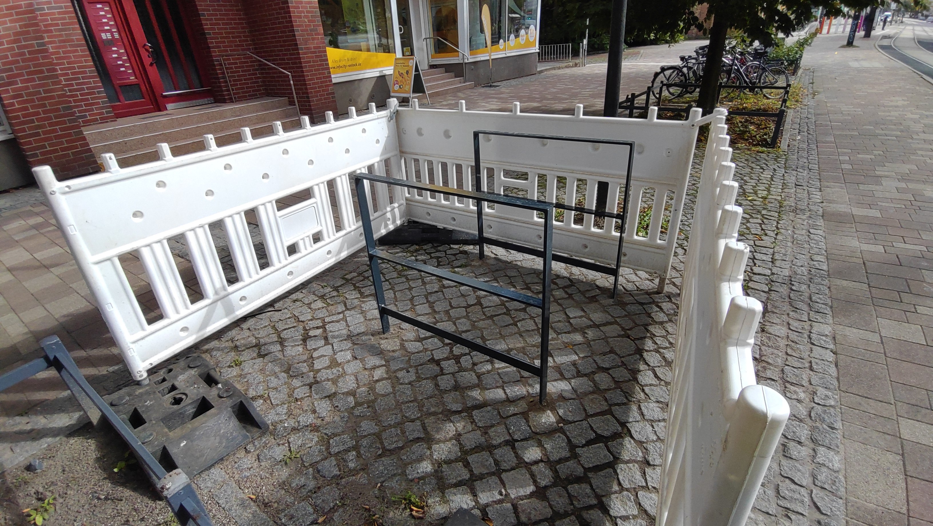 Mehrere weiße Fahrradständer aus Metall stehen auf einem gepflasterten Gehweg neben einem roten Backsteingebäude